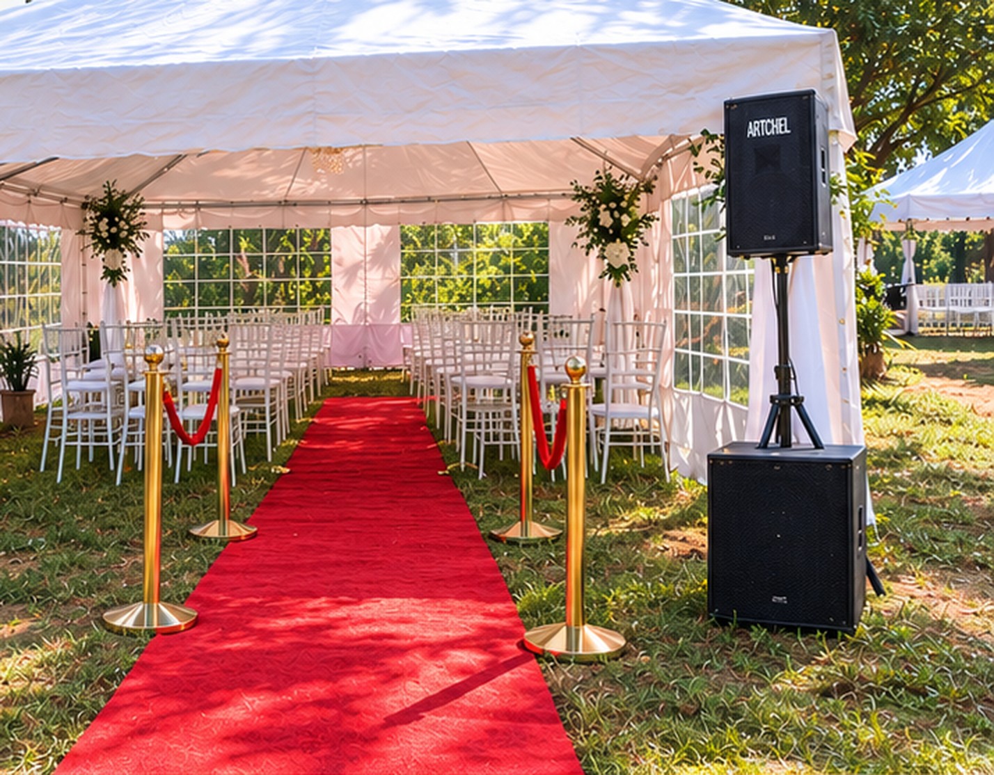 White event tent with Chiavari chairs, red carpet, gold stanchions and a speaker